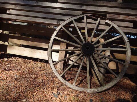 Antique wooden wagon wheel leaning against a wooden fence in the afternoon sun