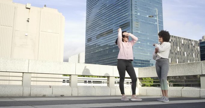 Diverse female friends performing stretching, jogging then moving laterally on rooftop for warm-up