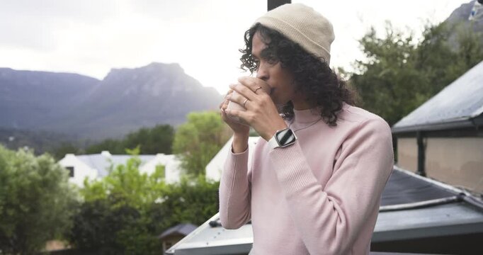 Morning mist inspiring non-binary person sipping from ceramic mug on balcony wearing knit beanie