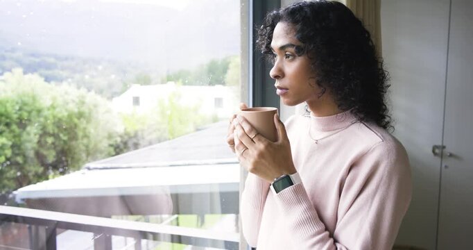 Non-binary person standing at window, cradling ceramic mug and sipping while reflecting, copy space