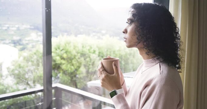 Person drinking coffee in pink sweater, smiling by sliding glass door