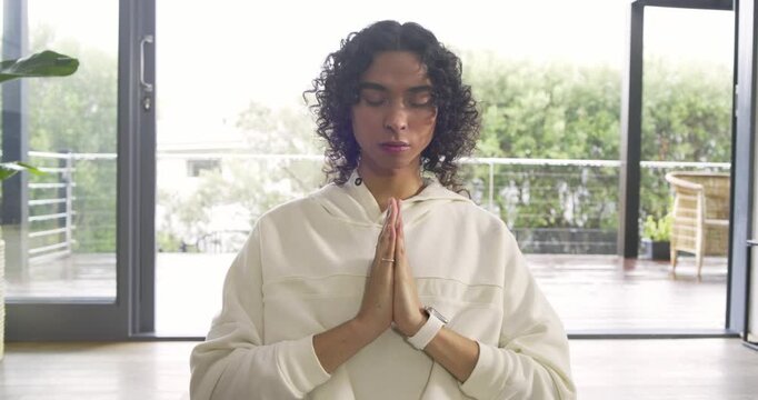 Closing eyes and pressing palms, non-binary adult meditating for calm in living room on yoga mat