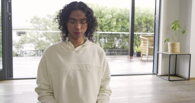 Non-binary person kneeling on yoga mat at home with smartwatch inhaling and exhaling for meditation