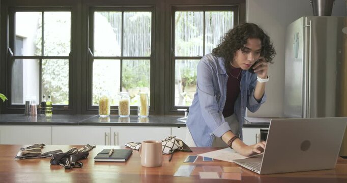 Nonbinary adult answering call while reading paper sorting swatches typing design notes in kitchen