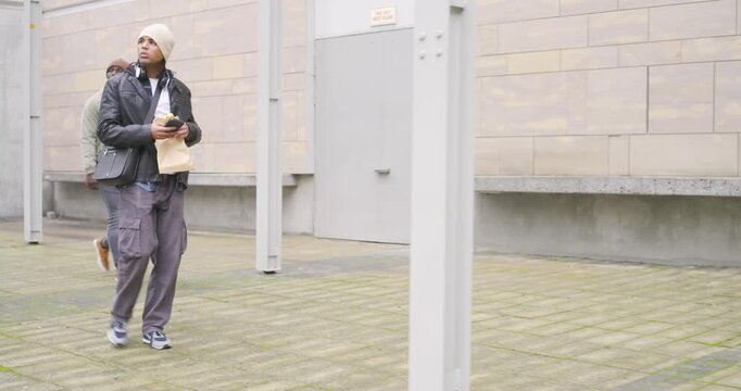 Carrying envelope and smartphone, African American man walking courtyard locating building entrance