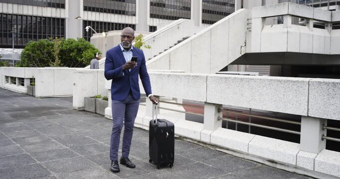 Upon arriving plaza African American businessman pulling suitcase typing phone seeking directions