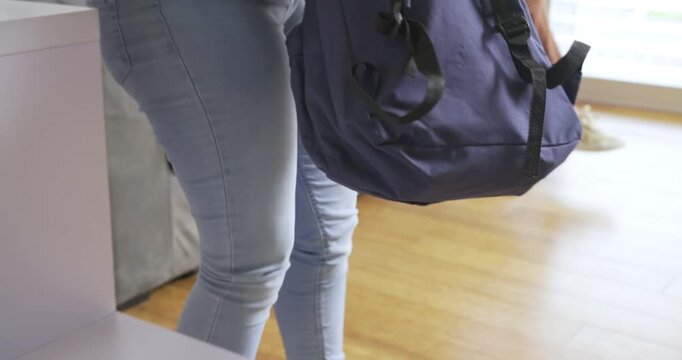 Noticing folder and case on table, daughter packing backpack with mother helping in living room