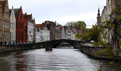 Naklejka premium Tourist boat cruising through the historic canals of Bruges with ancient brick architecture and stone bridge