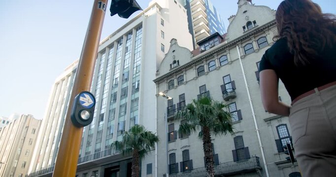 Woman pressing crossing button at intersection, activating signal and walking right carrying bag