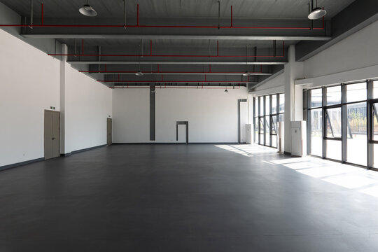 Spacious industrial-style indoor space with exposed ceiling pipes and large windows