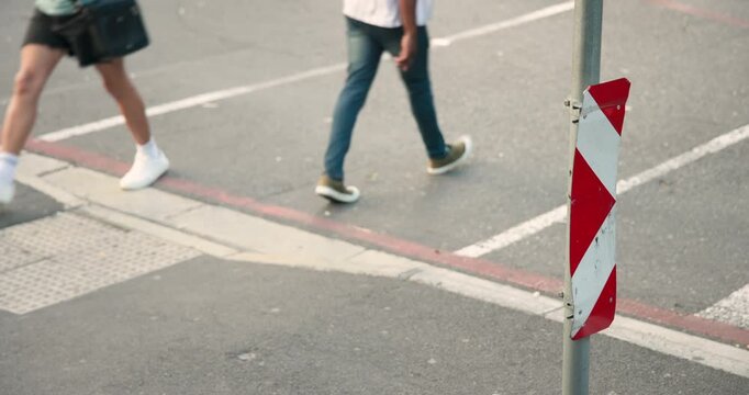 Diverse people entering from curb, crossing left past red-white chevron pole, commuting, copy space