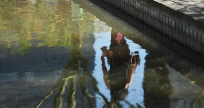 Diverse women leaning near reflecting pool creating ripples, walker passing bollard in sneakers