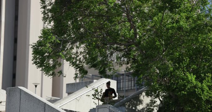 Campus concrete staircase is carrying commuters as single person is descending to plaza under tree