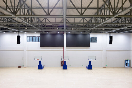 Indoor basketball gym with three hoops on wooden flooring and steel truss ceiling