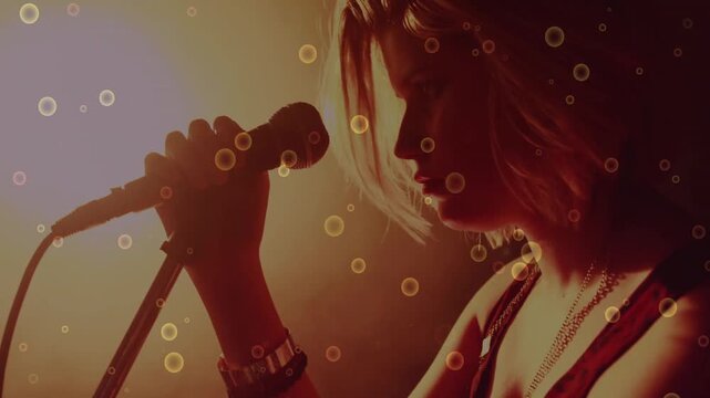 Female singer grabbing mic to lips, singing music amid amber light while circles overlaying profile