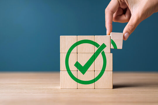 Completion and achievement concept. Abstract background with hand placing final wooden block to complete large green check mark symbolizing correctness, success, project management, and quality assura