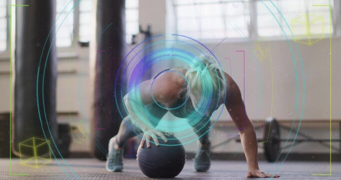 Vertical video: Woman in tank doing pushups on med ball at gym as HUD graphics pulsing for strength