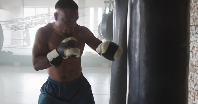 Male boxer leaning into heavy bag and building power, throwing short gloved hooks and jabs