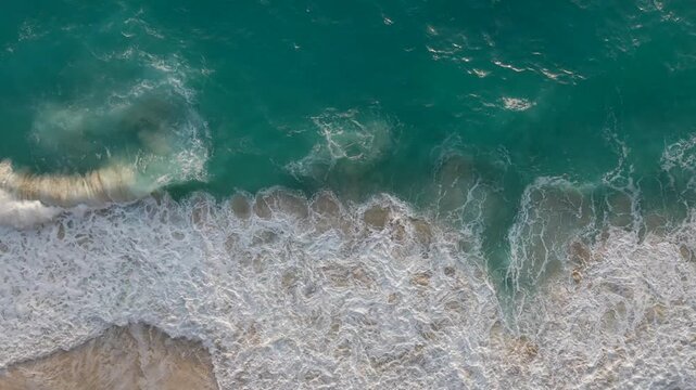 Powerful ocean waves crashing on sandy beach from above, dynamic tropical aerial view.