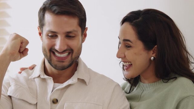 Hispanic couple using mobile device watching social media and winnning prize online at home on the sofa