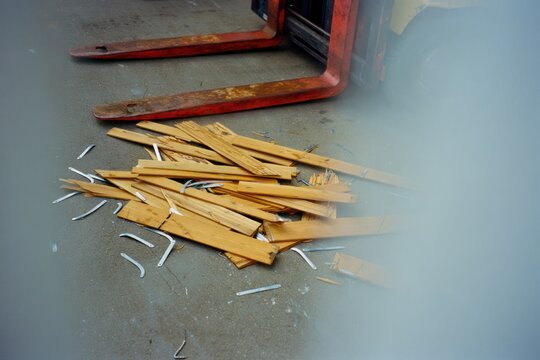 Broken wooden pallet pieces scattered on the ground near a forklift
