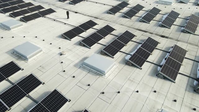 Drone view of rooftop solar panel arrays with visible wiring and lingering spring snow on a modern industrial building