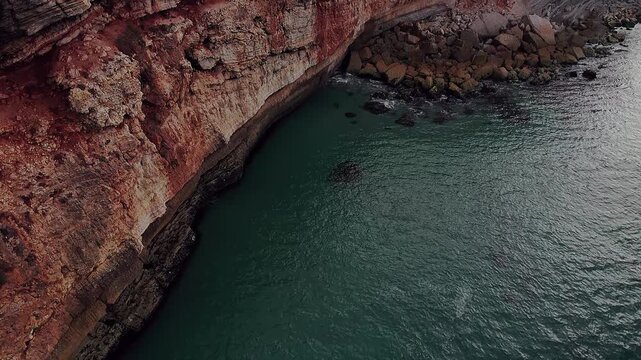 Drone view of eroded coastal cliffs in nazar&eacute; portugal, showing stratified rock layers, undercut formations and turquoise Atlantic water shaped by long-term marine erosion