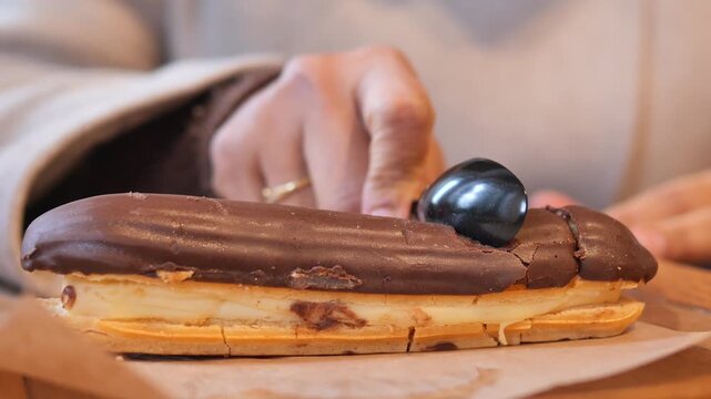 Close up slow motion of person cutting into chocolate eclair with a spoon on parchment paper