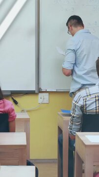 Vertical video: Teacher raising arm, writing and teaching at board while turquoise overlay crossing