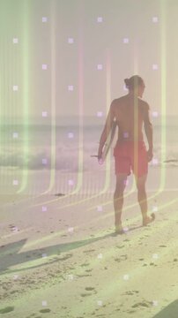 Vertical video: Surfer walking shore after surfing, holding board, leaving prints under light grid
