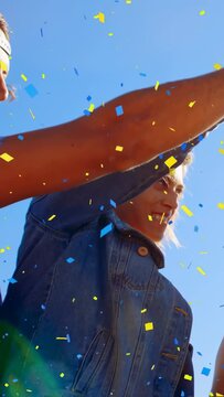 Vertical video: Falling confetti causing denim-clad adult raising beer and sipping under blue sky