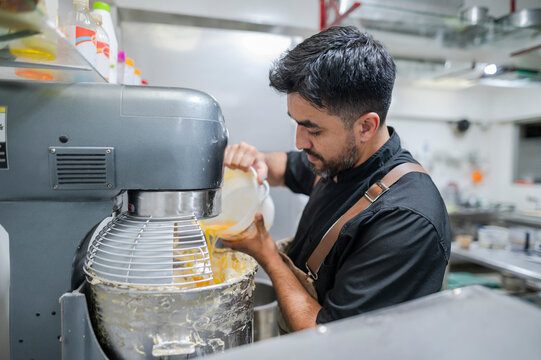 Latino baker pouring ingredients into a stand mixer