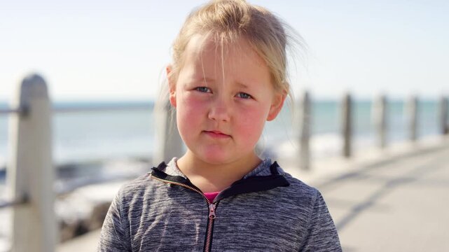 Beach, face and miserable with girl kid outdoor for holiday, travel or vacation frustration. Grumpy, moody and unhappy with child on promenade for getaway, sightseeing or tourism disappointment