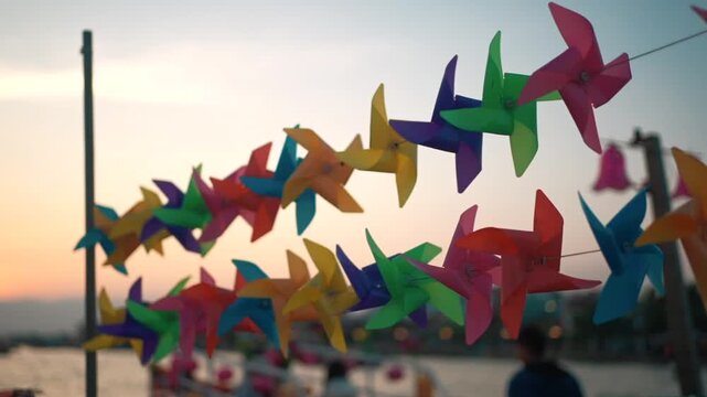 Colorful paper pinwheels spinning in wind during sunset boat travel on Asian river, Vibrant wind toys rotating on string above river cruise at evening Vietnam journey scene