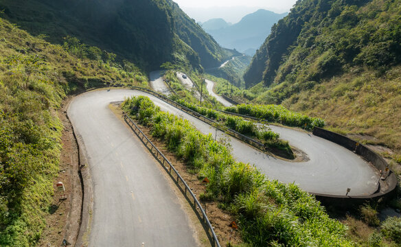 Motorcyclists navigate the winding mountain roads of Doc Tham Ma Pass, Dong Van, Ha Giang, Vietnam. The steep terrain and lush greenery make it a popular destination for adventure tourism.