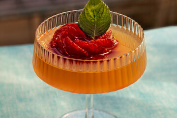 Orange juice cocktail served in champagne glass with raspberry ice in rosette shape and fresh green mint leaf. Summer refreshment drink for celebration and relaxing beverage concept. © Lassi M