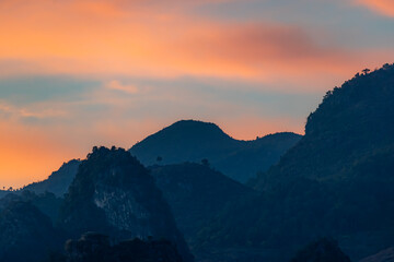 Obraz premium A scenic view of the silhouette of mountains against a colorful sky at dusk in TDong Van, Ha Giang, Vietnam. The landscape is serene and peaceful.