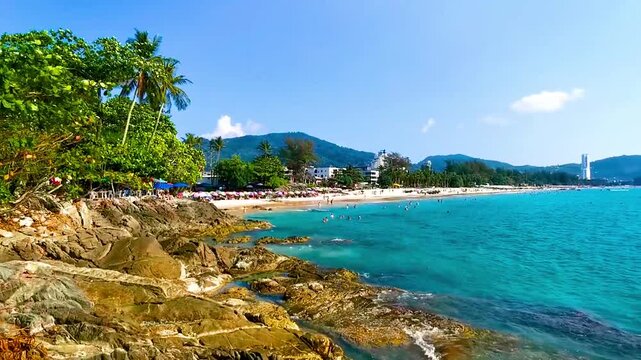 Tropical Patong Beach Phuket Thailand people tourists parasol palms rocks.
