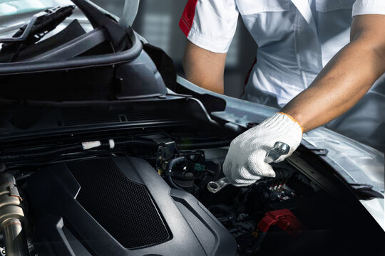 Close-up of a professional car mechanic wearing gloves using a wrench to inspect and maintain a vehicle engine in an auto repair garage. Concept of automotive service, maintenance, repair work, and ve