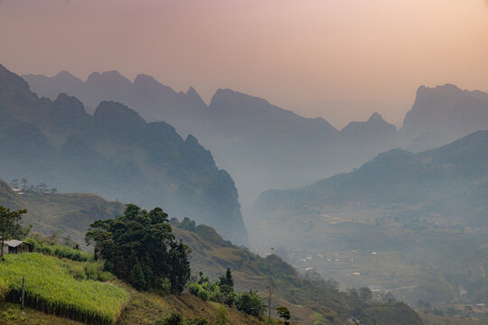 A scenic view of the mountains in Lung Ho, Yen Minh, Ha Giang, Vietnam, showcasing the natural beauty of the region. The landscape features rolling hills and a small village below.