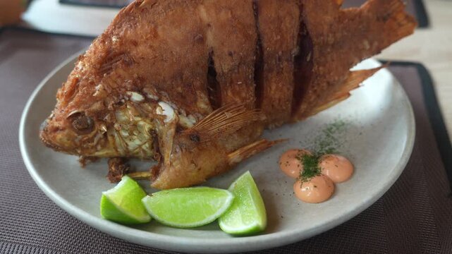 Close-up of a crispy whole fried mojarra fish plate with lime wedges