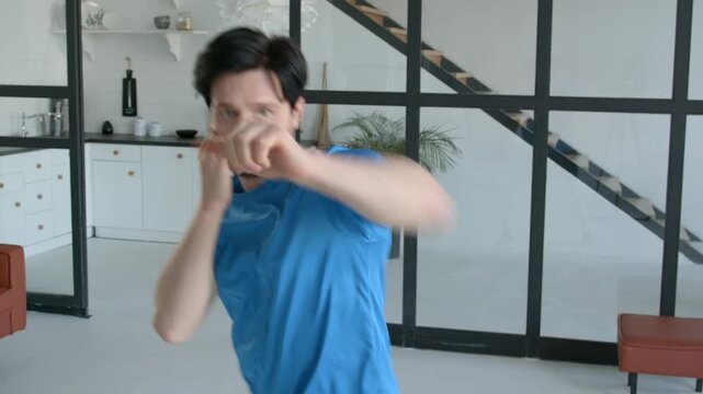 Portrait of active sporty muscular build man practicing shadow boxing workout, training punching techniques, improving upper and lower body muscles at home.