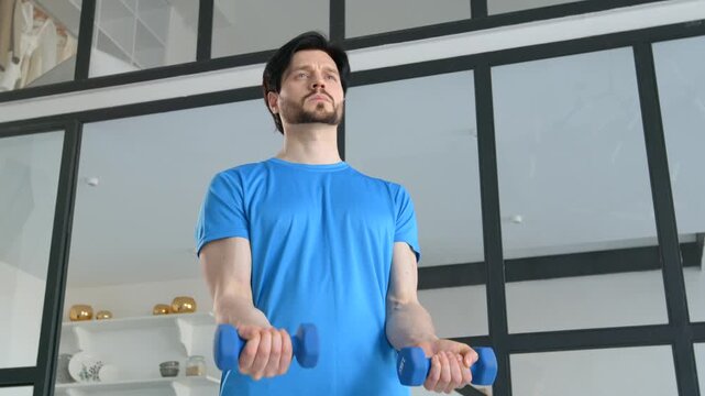 Portrait of active determined sporty fit man exercising dumbbell biceps curl, strengthening upper arm, expressing determination and confidence while working out at home.