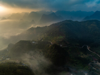 Naklejka premium An aerial view shows the winding roads and misty mountains of Dong Van, Ha Giang, Vietnam, as the sun rises, creating a scenic and ethereal landscape at dawn.
