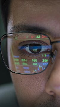 Close-up of eye with glasses reflecting stock market trading data, vertical footage