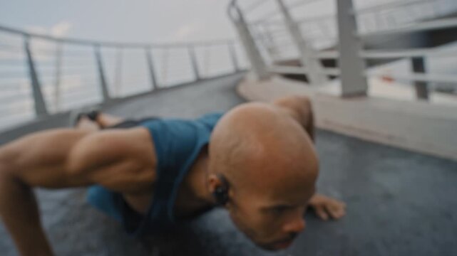 Man, push ups and earphones in city for fitness with strength training, audio and listen to music on bridge. African person, exercise and outdoor with streaming service, strong and workout in town