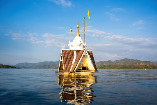 A floating pagoda peacefully standing in the middle of a vast reservoir surrounded by mountain ranges in Kanchanaburi, Thailand.