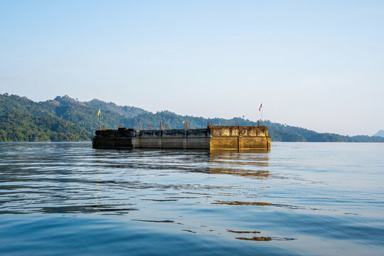A partially submerged concrete structure standing in the reservoir with distant mountain ranges in Kanchanaburi, Thailand.