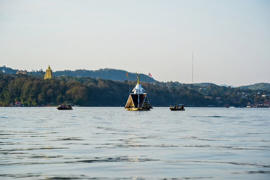 Two long-tail boats filled with tourists heading toward a floating shrine in calm waters with forest and temple in the background