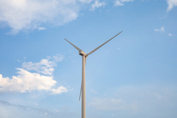 Fototapeta premium Single wind turbine against clear blue sky with soft clouds, minimal composition highlighting renewable energy and clean power generation in modern sustainable environment.